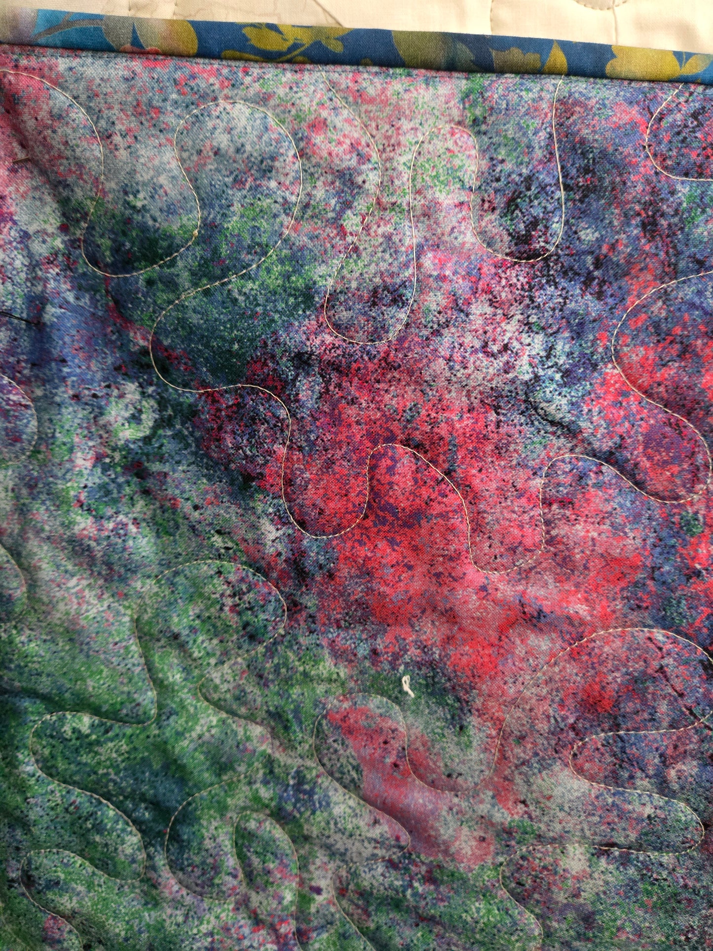 Textured fabric with abstract patterns in red, green, pink, purple and blue. Quilting stitch displayed